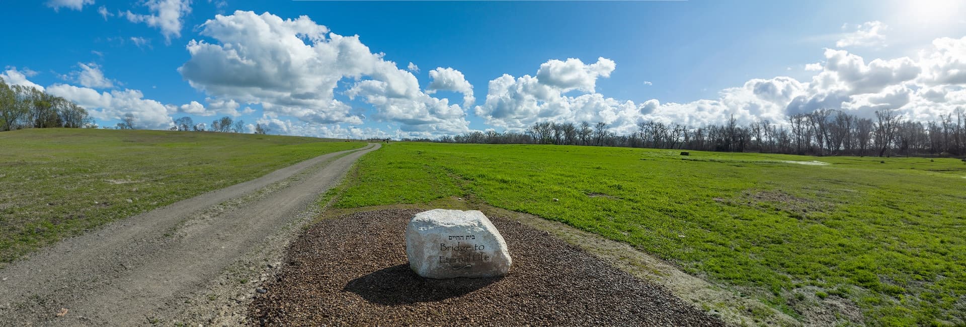 Panoramic view of a meadow trail and natural boulder marker at a green cemetery in Placer County