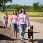 Family walking with Doberman on sunny rural path