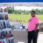Vendor smiles beside colorful handmade crafts at outdoor market