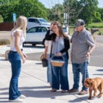 Three adults chatting in a sunny parking lot with dog