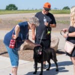 Elderly woman pets black dog with others watching outdoors