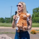 Woman holding plush toy and speaking into microphone outdoors