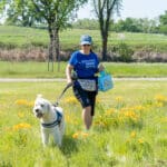 Woman walking dog in sunny field of wildflowers