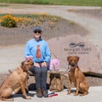Woman seated with two dogs near Morgan Oaks sign