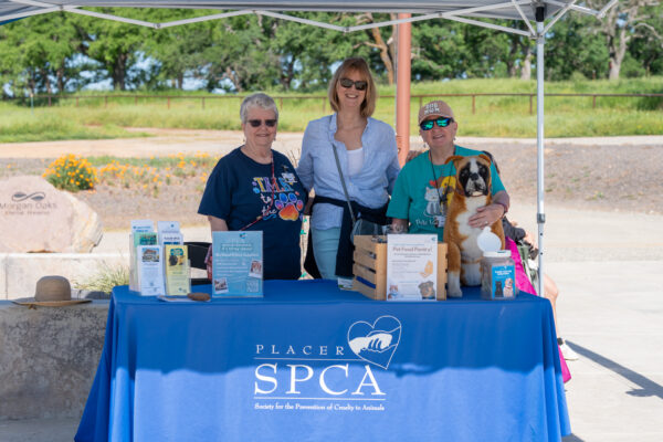 Volunteers at a Placer SPCA event table with dog