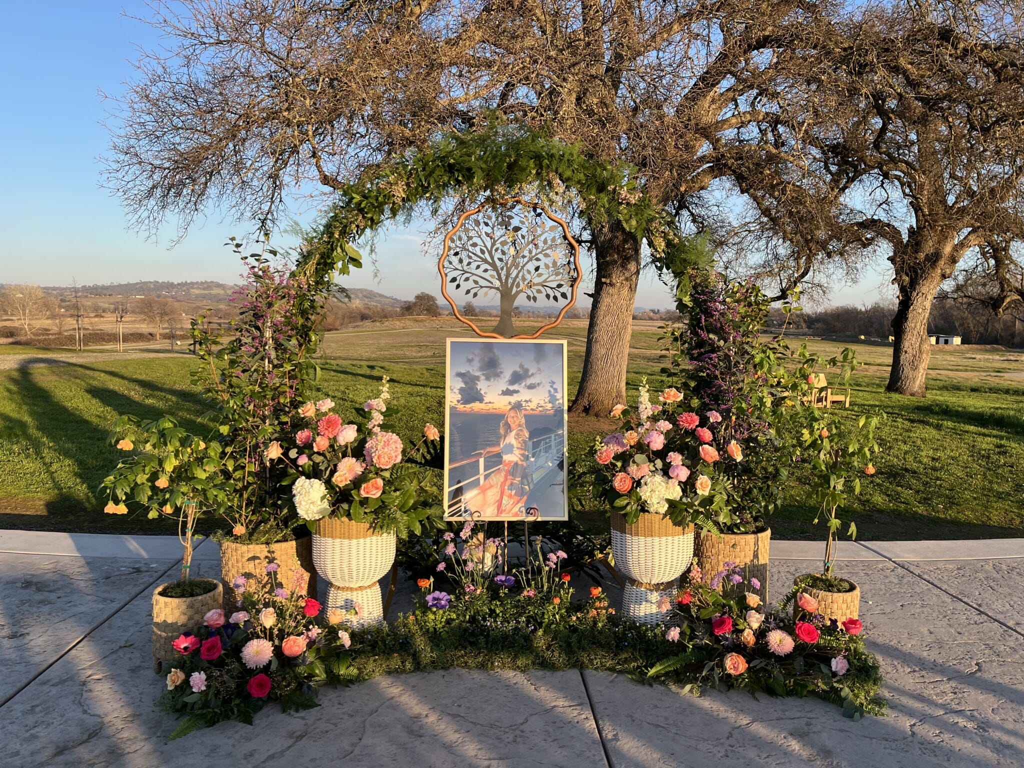 Outdoor floral memorial setup with trees under sunny sky